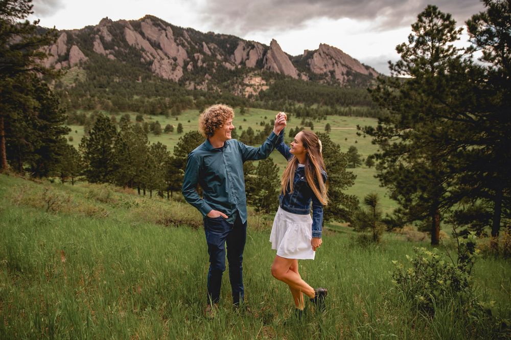 Two people stand in a meadow with scenic Flatirons rock formations and mountains of Boulder, Colorado in the background.