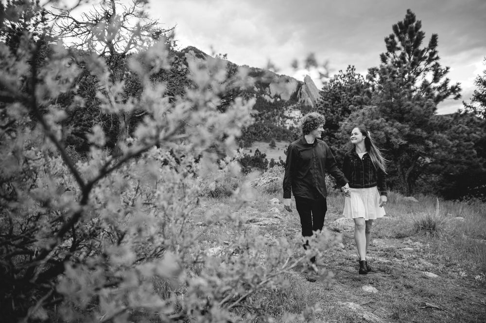 A couple walks hand in hand along a mountain trail surrounded by blooming spring foliage in black and white.