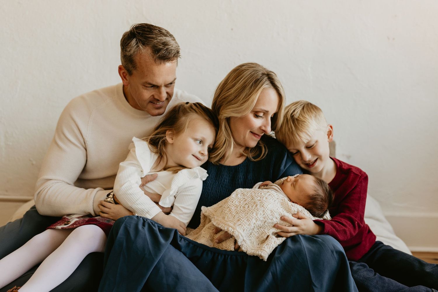 Cozy family moment sitting together on sofa with newborn baby in muted neutral tones. Tulsa newborn photographer.
