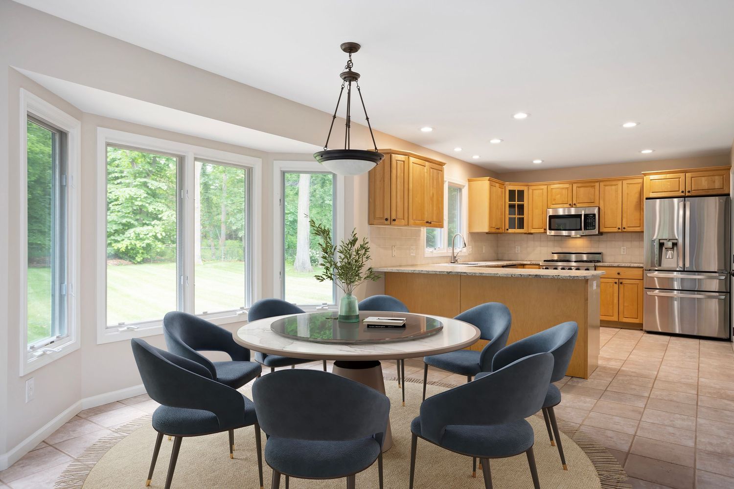 Virtually staged dining area with round table, modern velvet chairs, natural light, and open-concept kitchen with wood cabinetry.