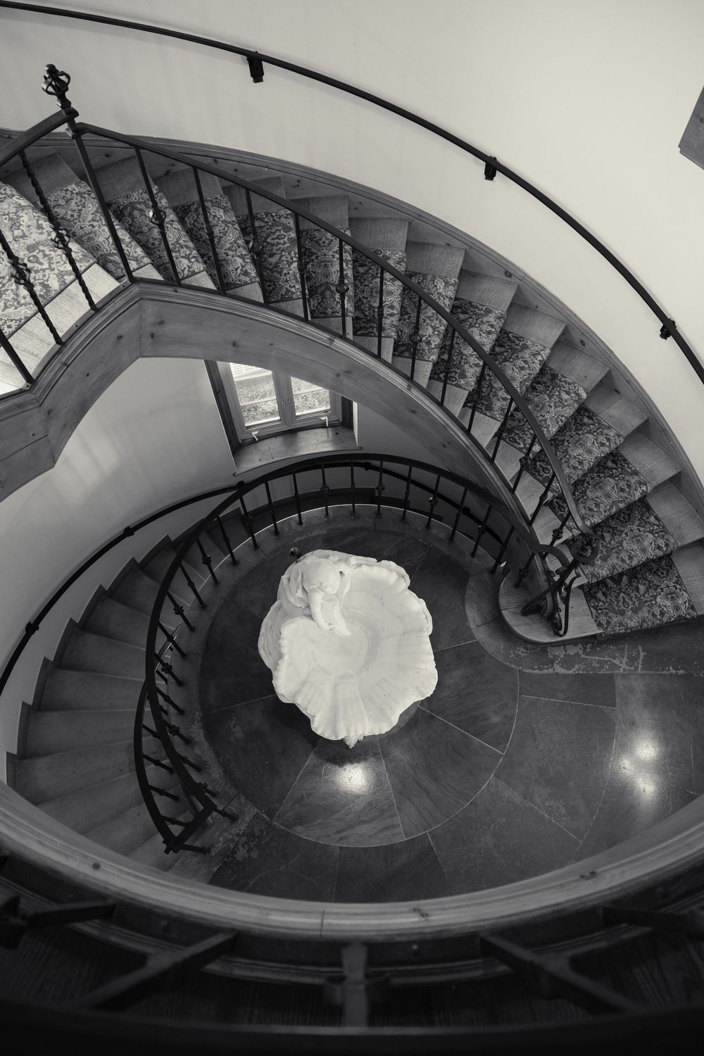 A dramatic black and white spiral staircase shot from above with a white wedding dress creating a circular pattern below.