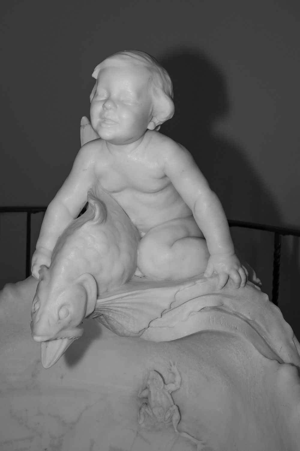 White marble sculpture of a cherubic child figure in a reclining pose against dark background.