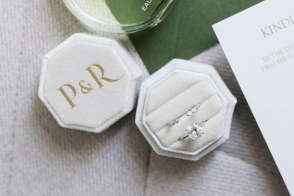 Wedding rings and monogrammed P&R jewelry boxes styled on green and white surface.