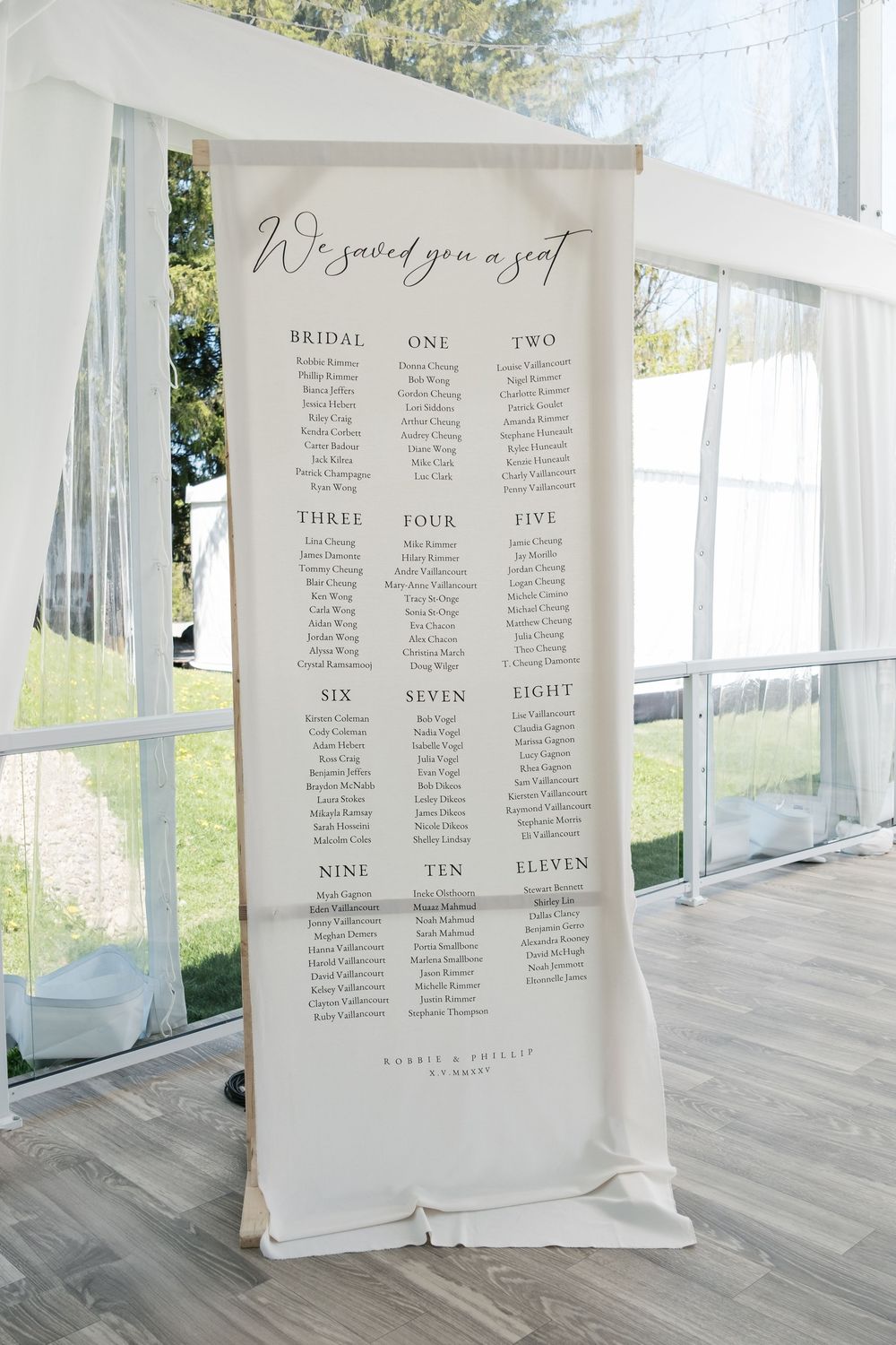 Elegant wedding seating chart display on white fabric banner in outdoor venue.