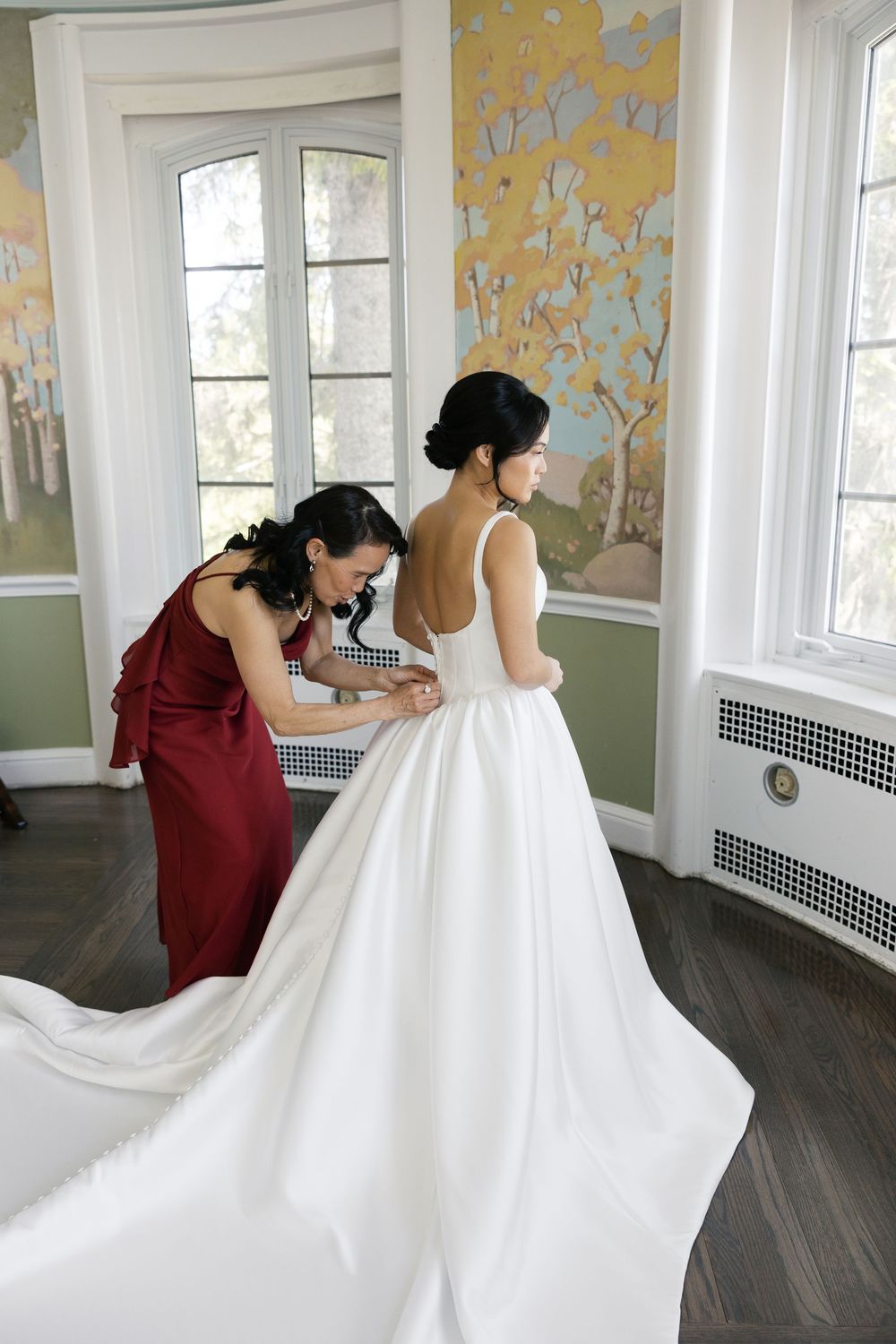 Wedding dress preparation scene in a room with yellow floral wallpaper and bright bay windows.