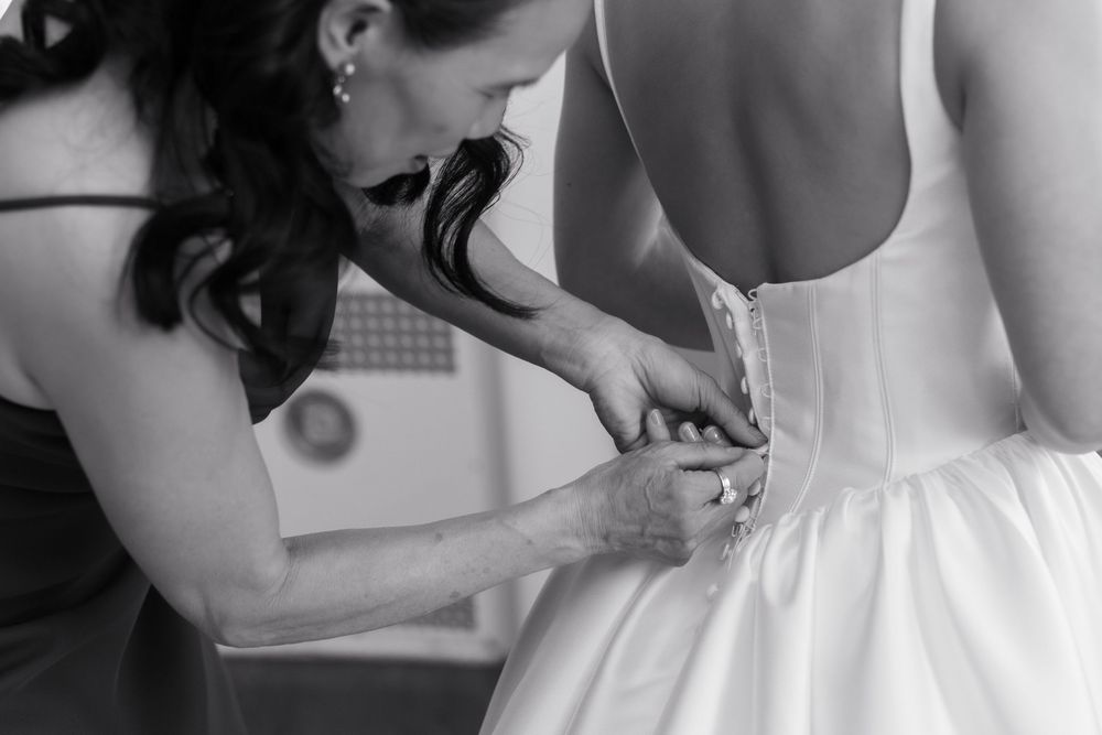 Black and white photo of wedding dress being buttoned up during bridal preparations.