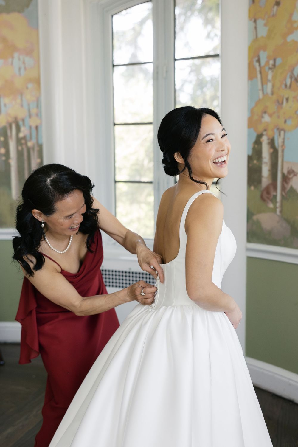 Wedding dress fitting moment in elegant room with nature-inspired wallpaper.