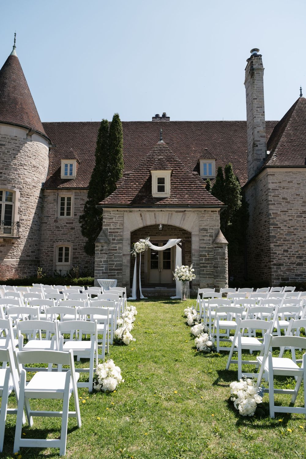Stone castle wedding venue with white chairs and floral aisle decor set up for outdoor ceremony.