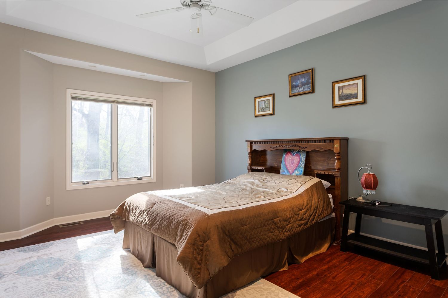 Cozy bedroom with gray walls, wooden headboard, and large windows offering natural light.