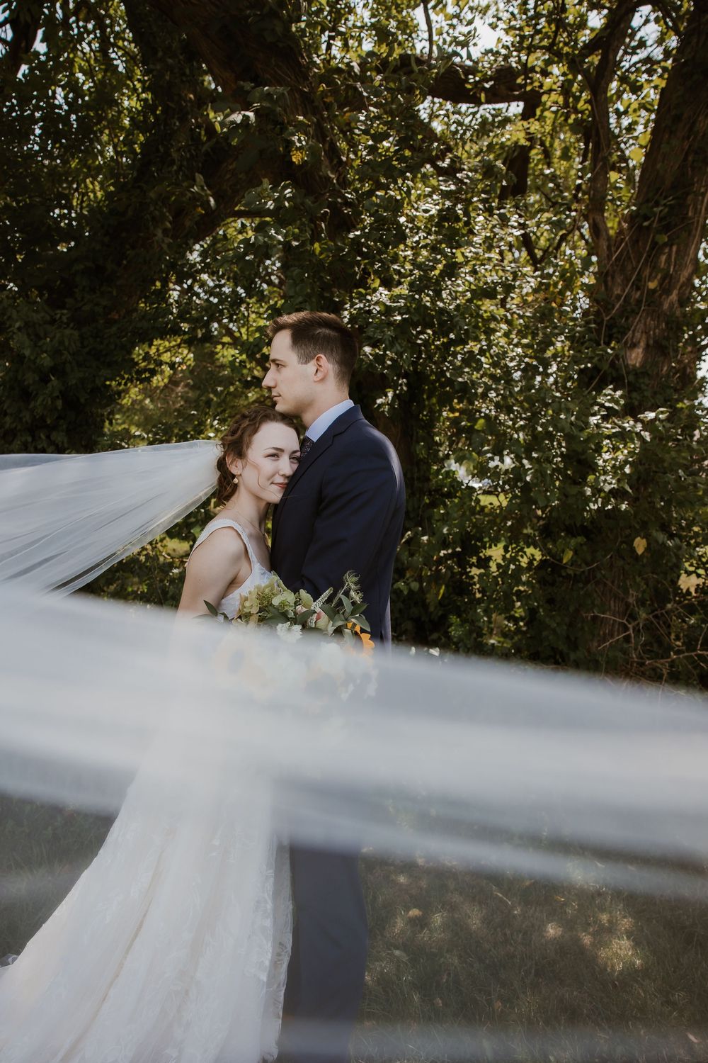 A romantic wedding photo shows a couple embracing outdoors with a flowing veil in the foreground.