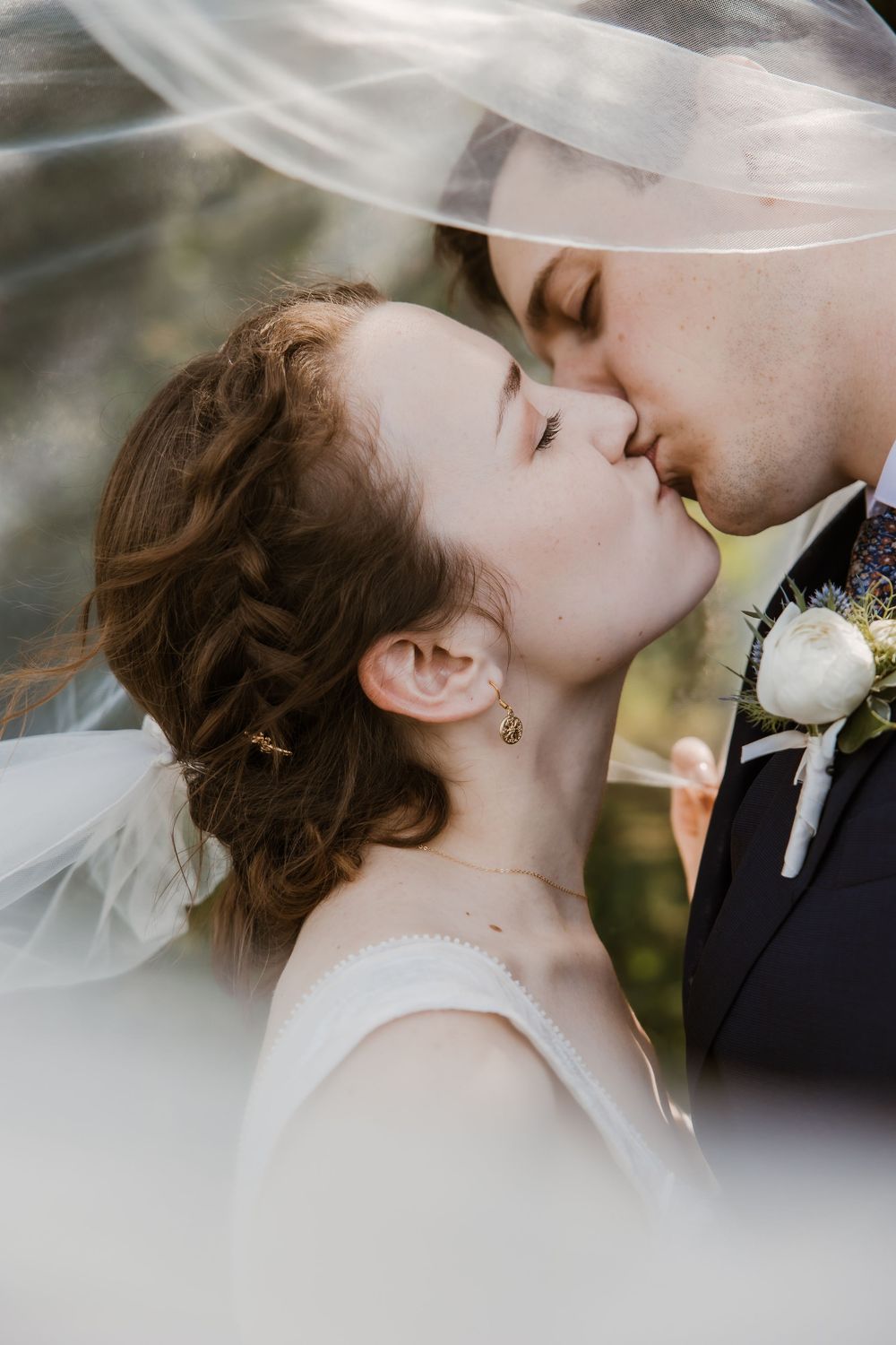 A a couple in an intimate kiss under flowing veil with white boutonniere detail. Golden hour in Meadowbrook Park in Prairie village Kansas.