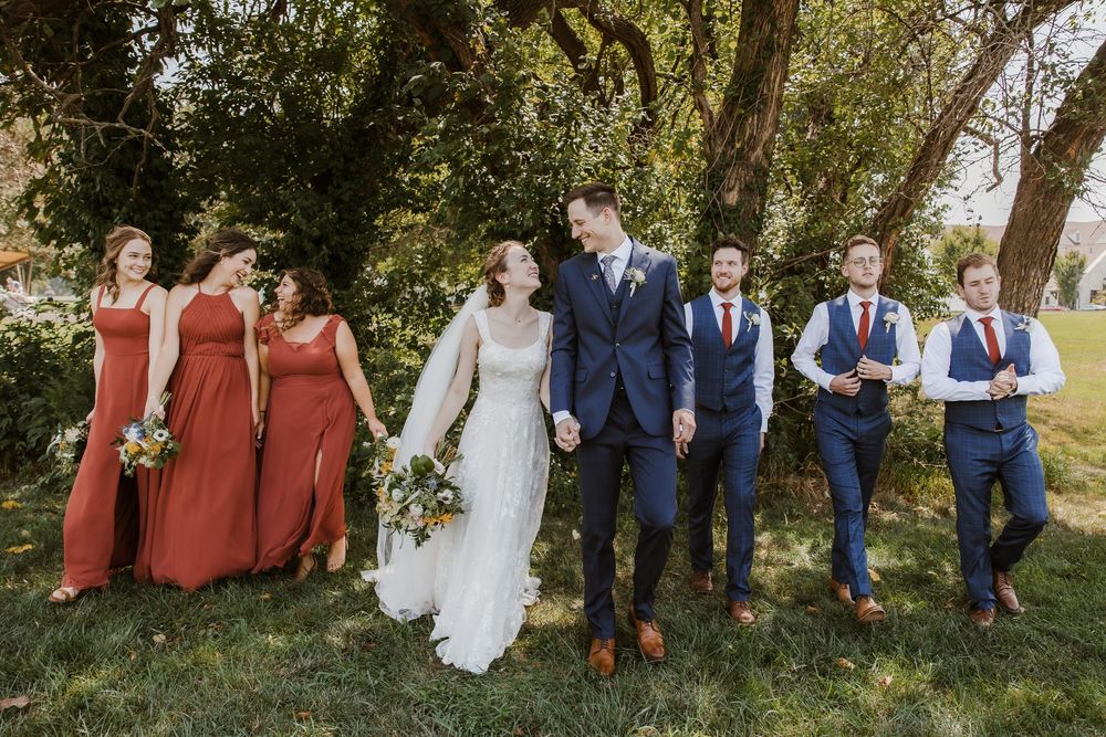 Elegant bridesmaids in rust dresses and groomsmen in navy suits at Meadowbrook Park wedding photos in Prairie Village.