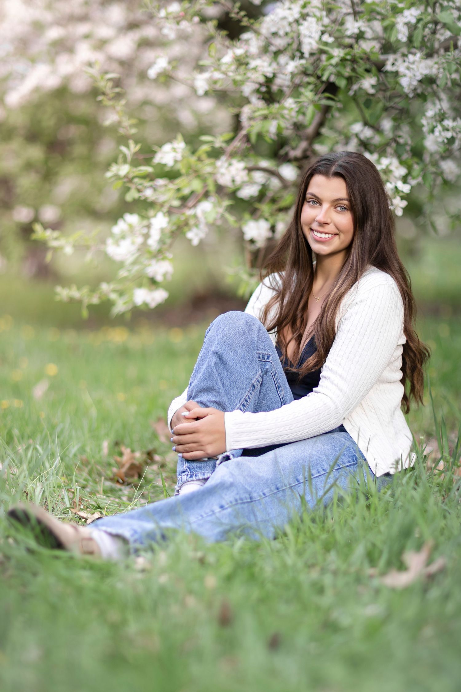 Senior girl smiling under apple blossoms during spring portrait session in Berrien County, Michigan