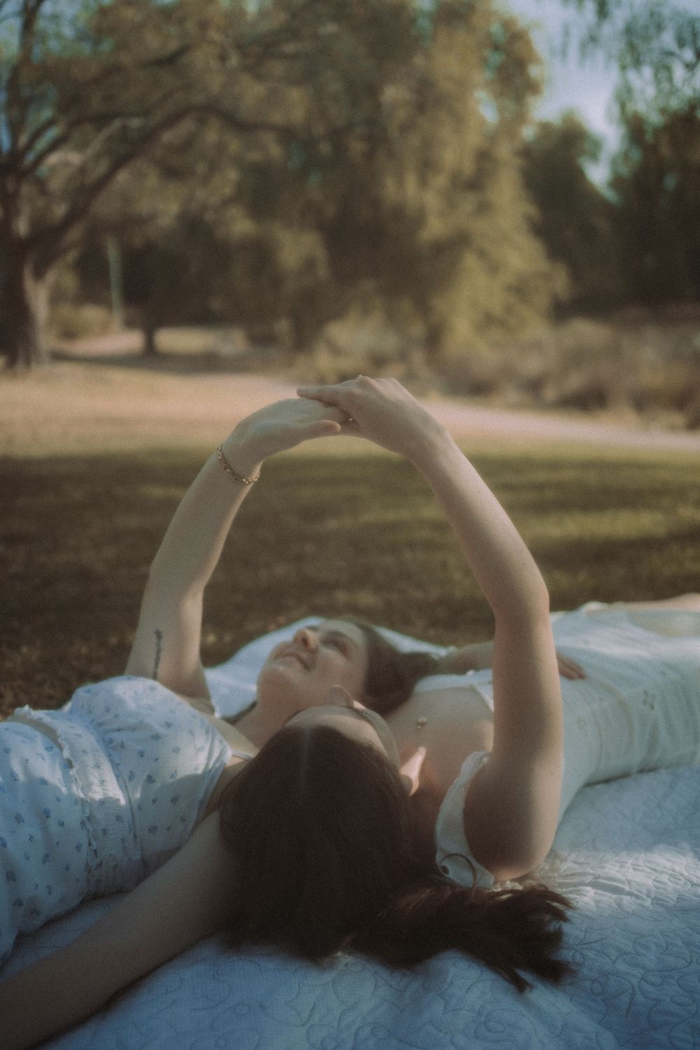 Person lying on white blanket outdoors stretching arms up against dreamy natural background.