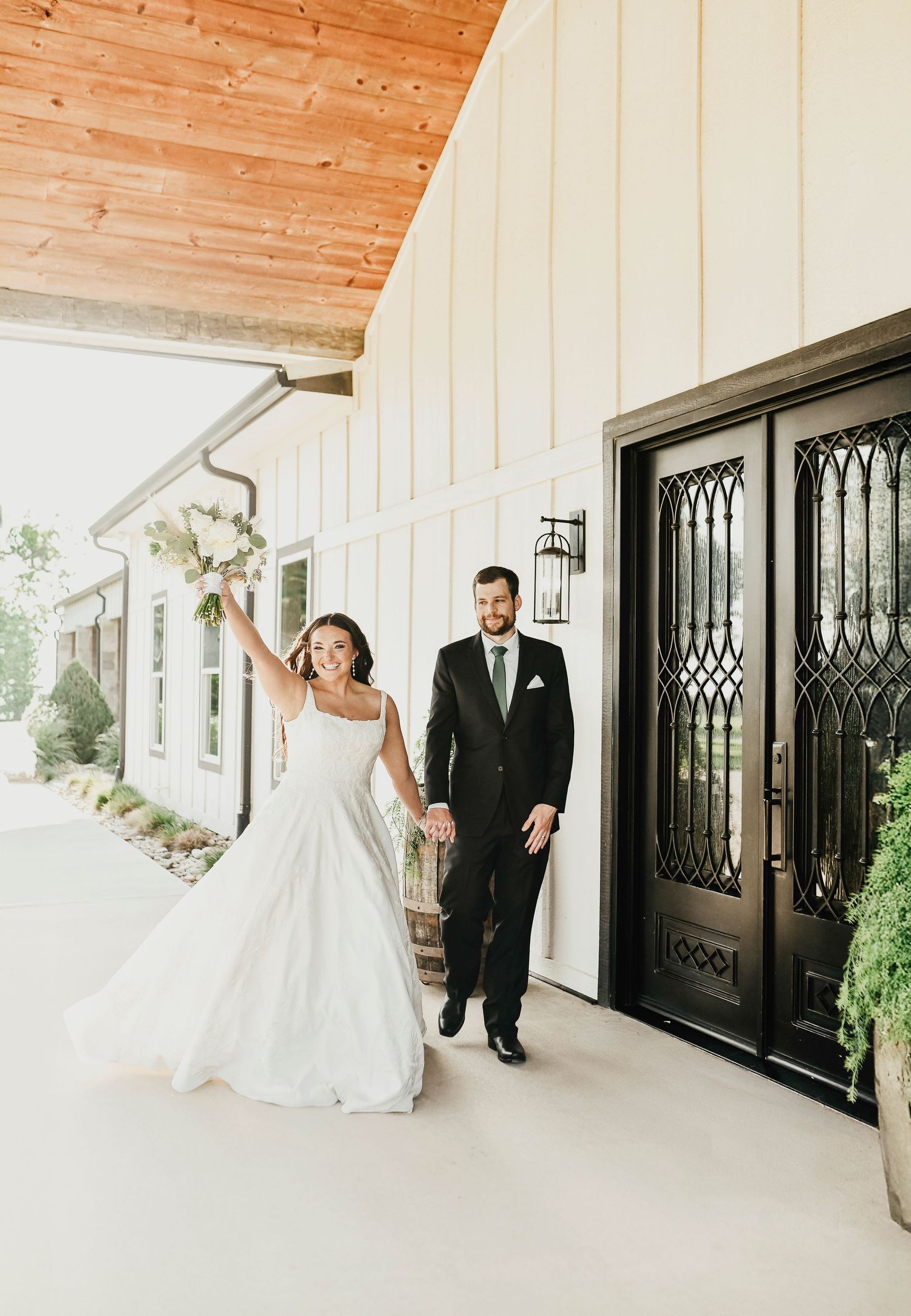 Bride holding bouquet beside groom in front of The Madelyn barn