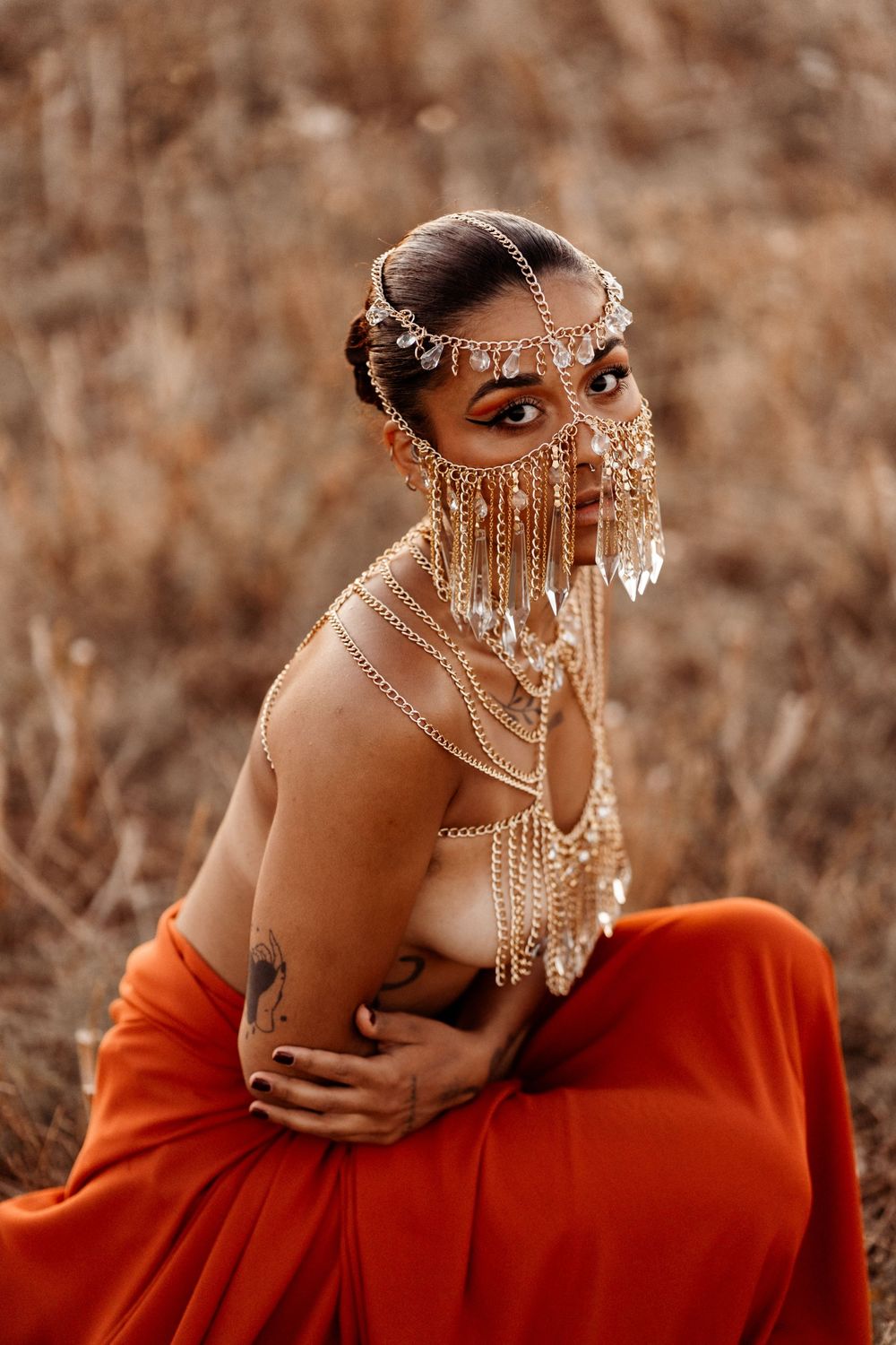 Figure in orange dress wearing ornate silver jewelry and beaded headpiece in ethereal autumn portrait setting.