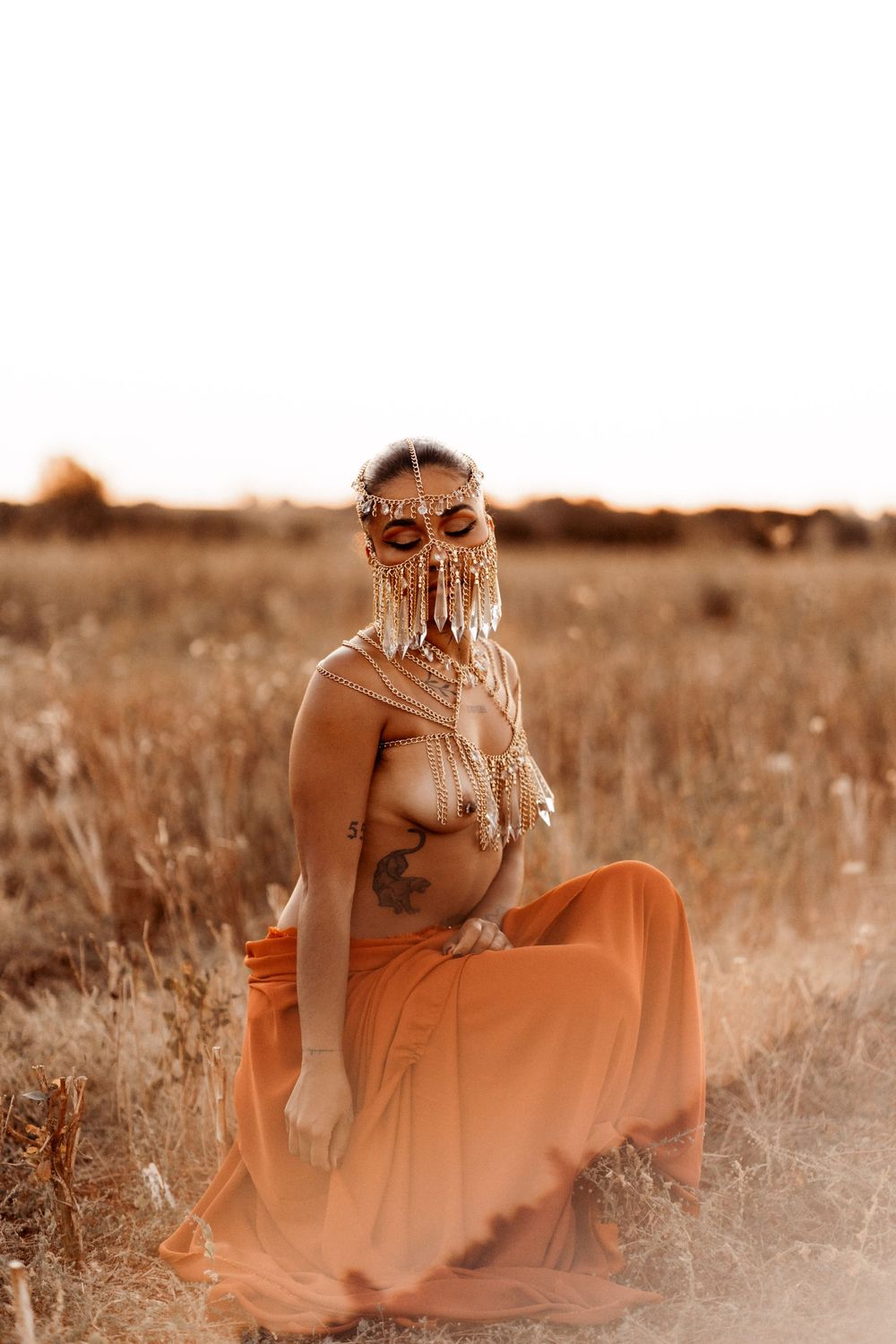 Woman in flowing orange dress poses in sepia-tinted field during golden hour photoshoot.