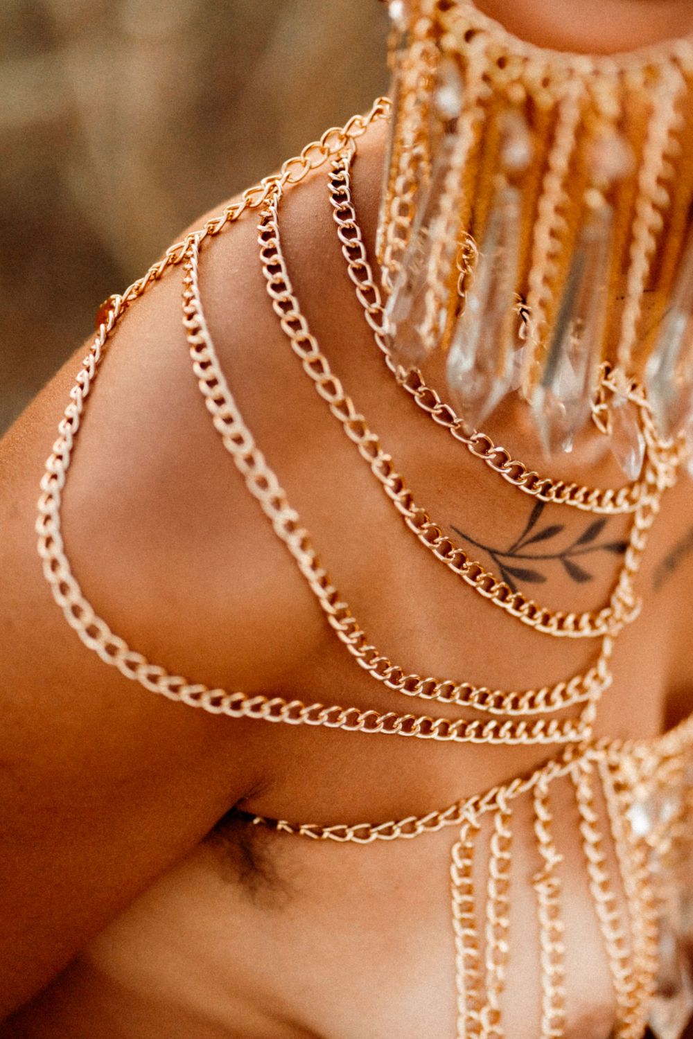 Delicate gold chain jewelry draped across skin in cascading layers with soft warm lighting.
