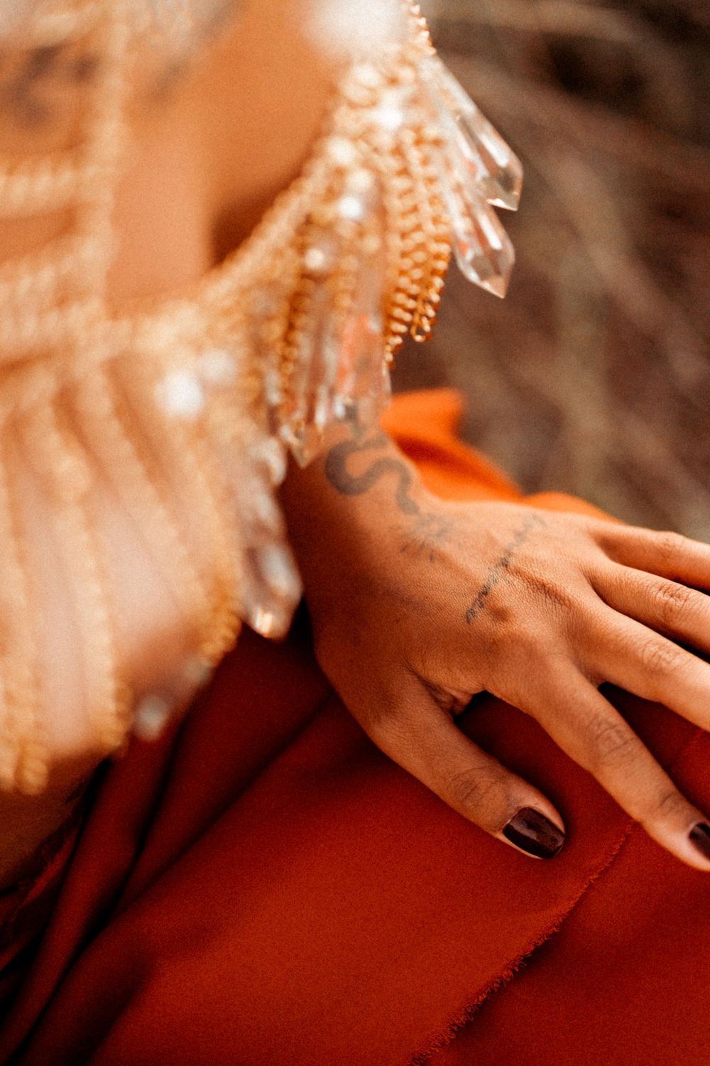 Hand with black nail polish and small tattoos wearing sparkly beaded formal wear against a red background.