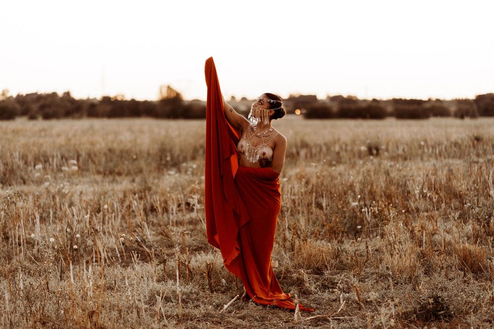 A figure in a flowing red dress stands gracefully in a sepia-toned field during golden hour.