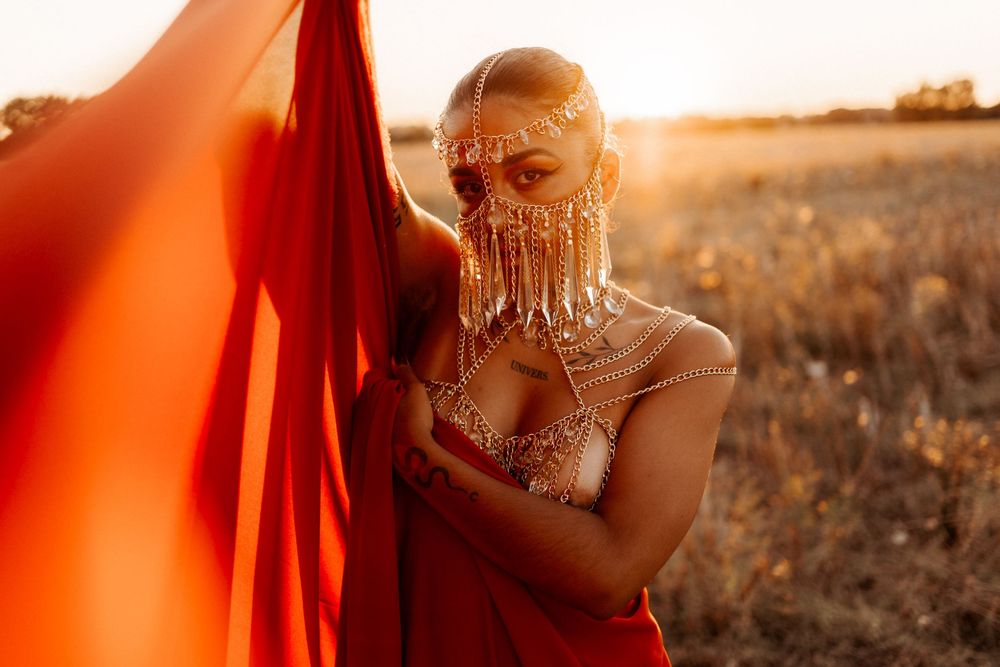 Beautiful portrait in golden sunset light with flowing red fabric and ornate jewelry in a field at golden hour.