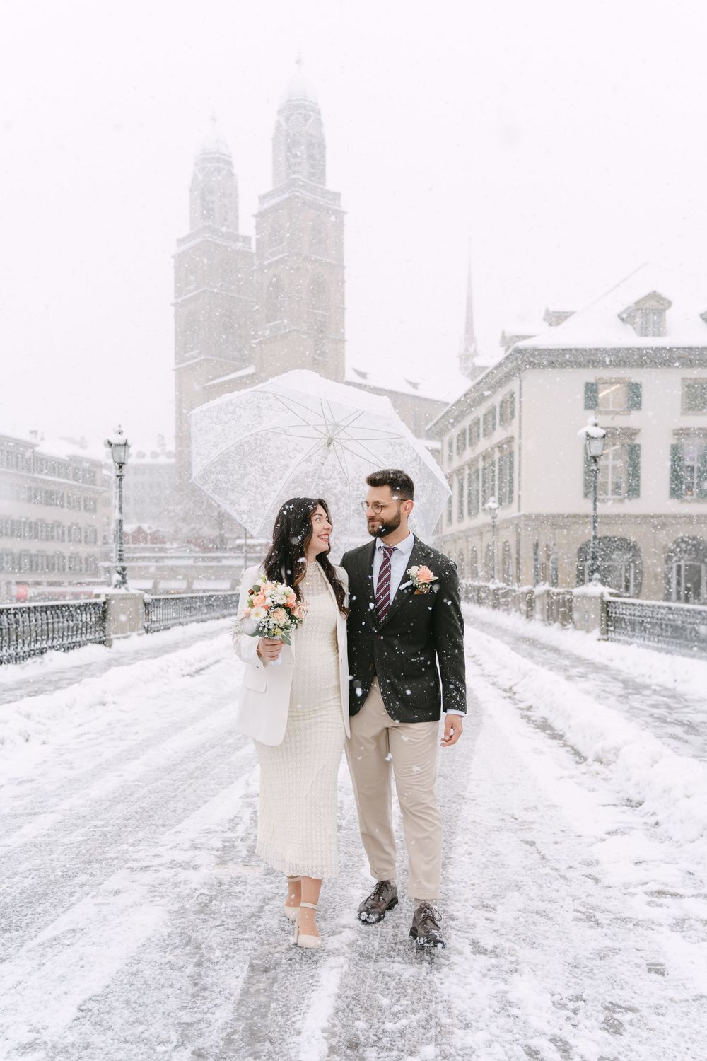 A couple shares a romantic winter moment with white church spires in Zurich during snowfall.