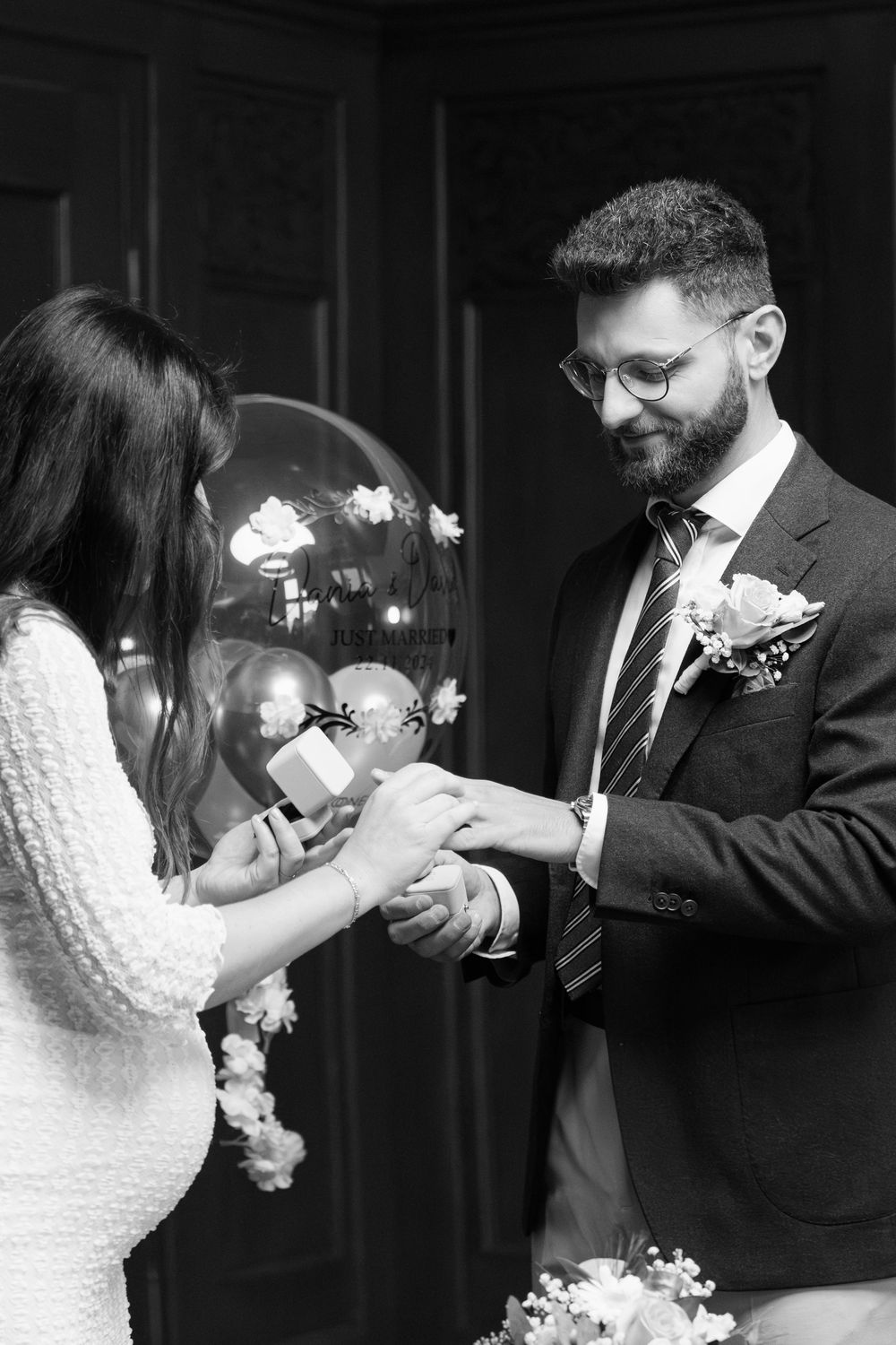 A black and white photo of a wedding ceremony moment as rings are exchanged during an intimate indoor celebration.