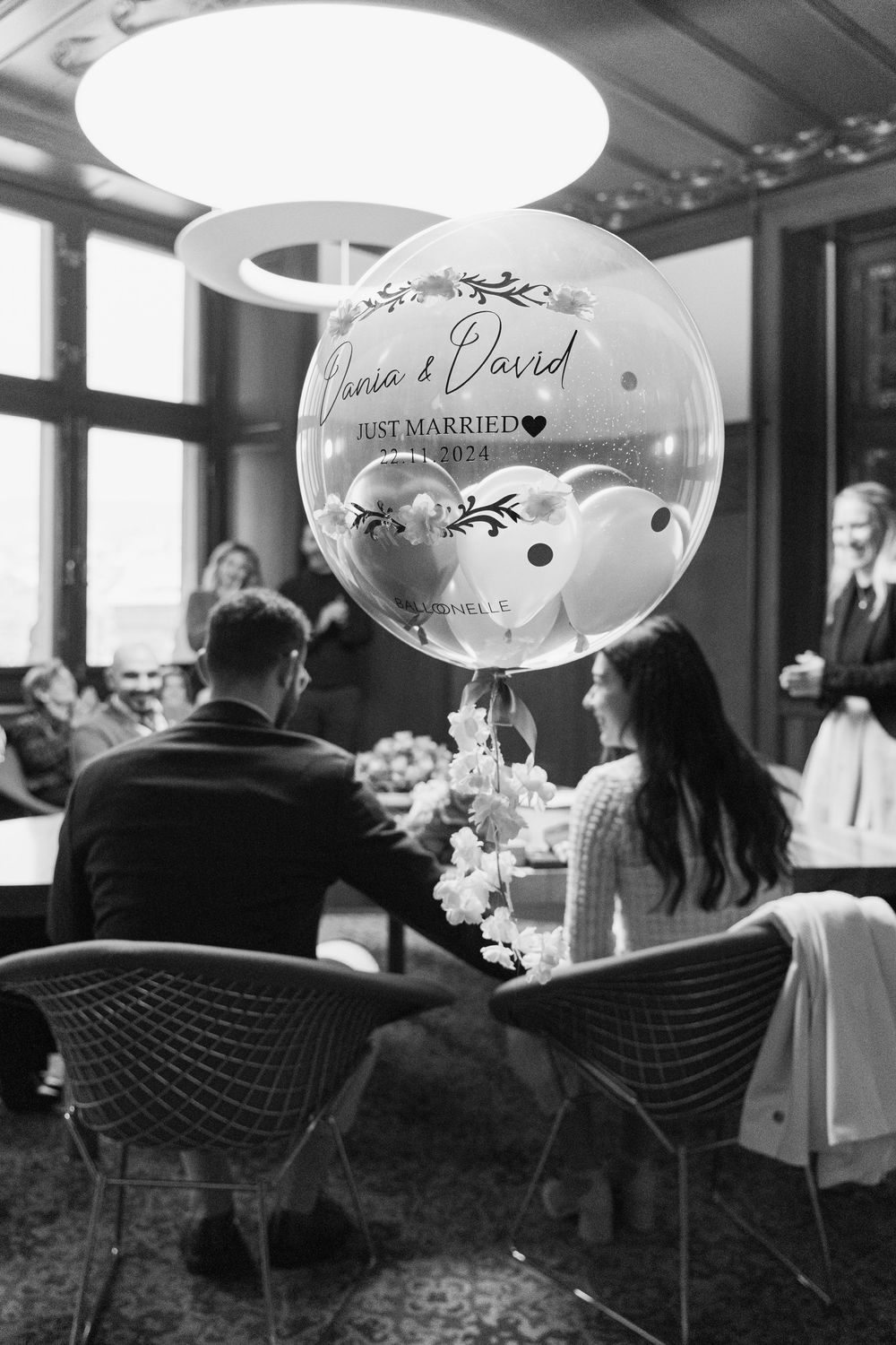 A transparent balloon with 'Just Married' text floats above a table at a wedding reception, captured in black and white.