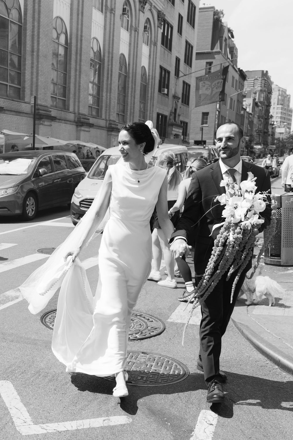 A couple walking down a city street during a wedding celebration with flowers and flowing dress in black and white.