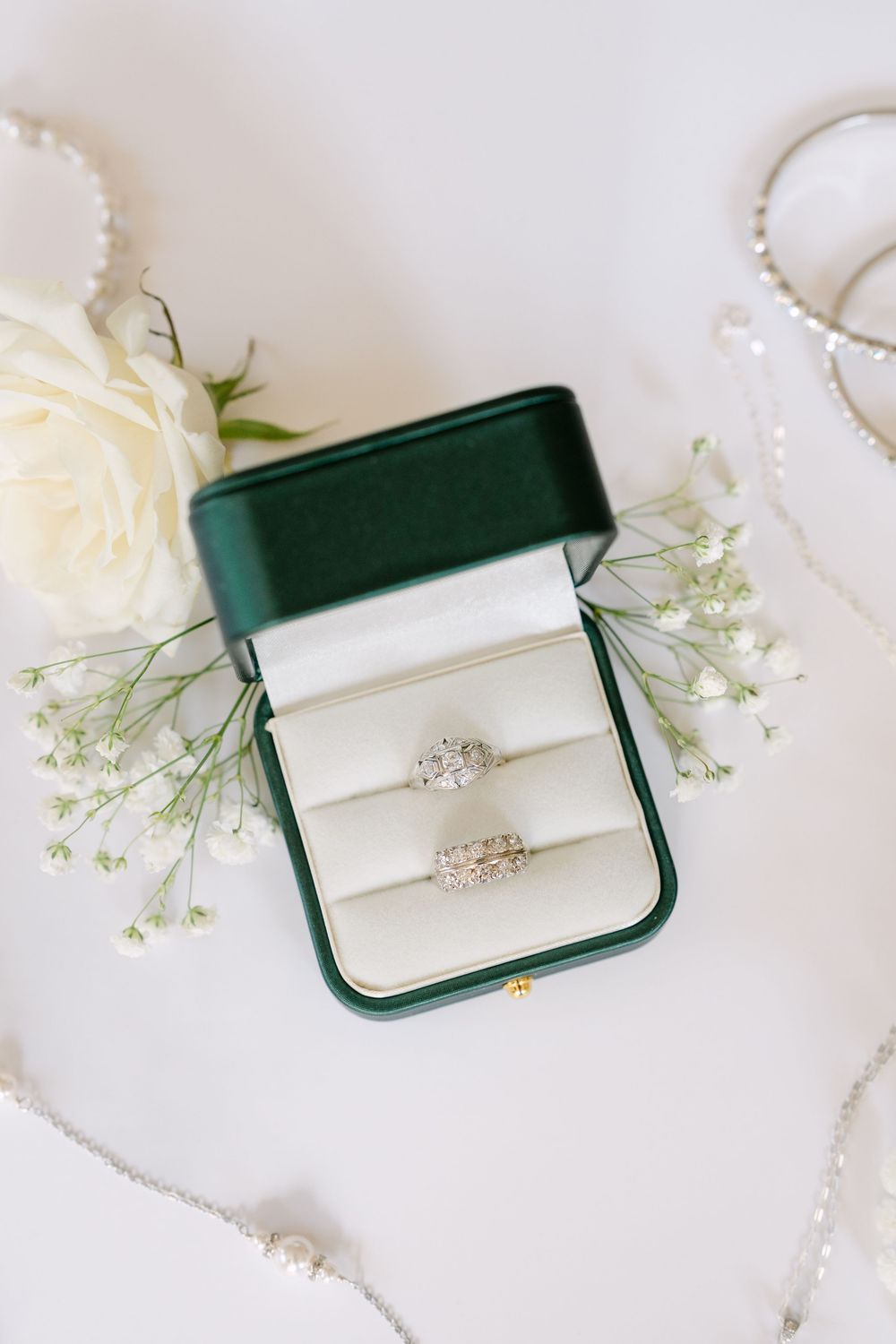 Elegant engagement rings displayed in dark green jewelry box with white roses and delicate baby's breath flowers.