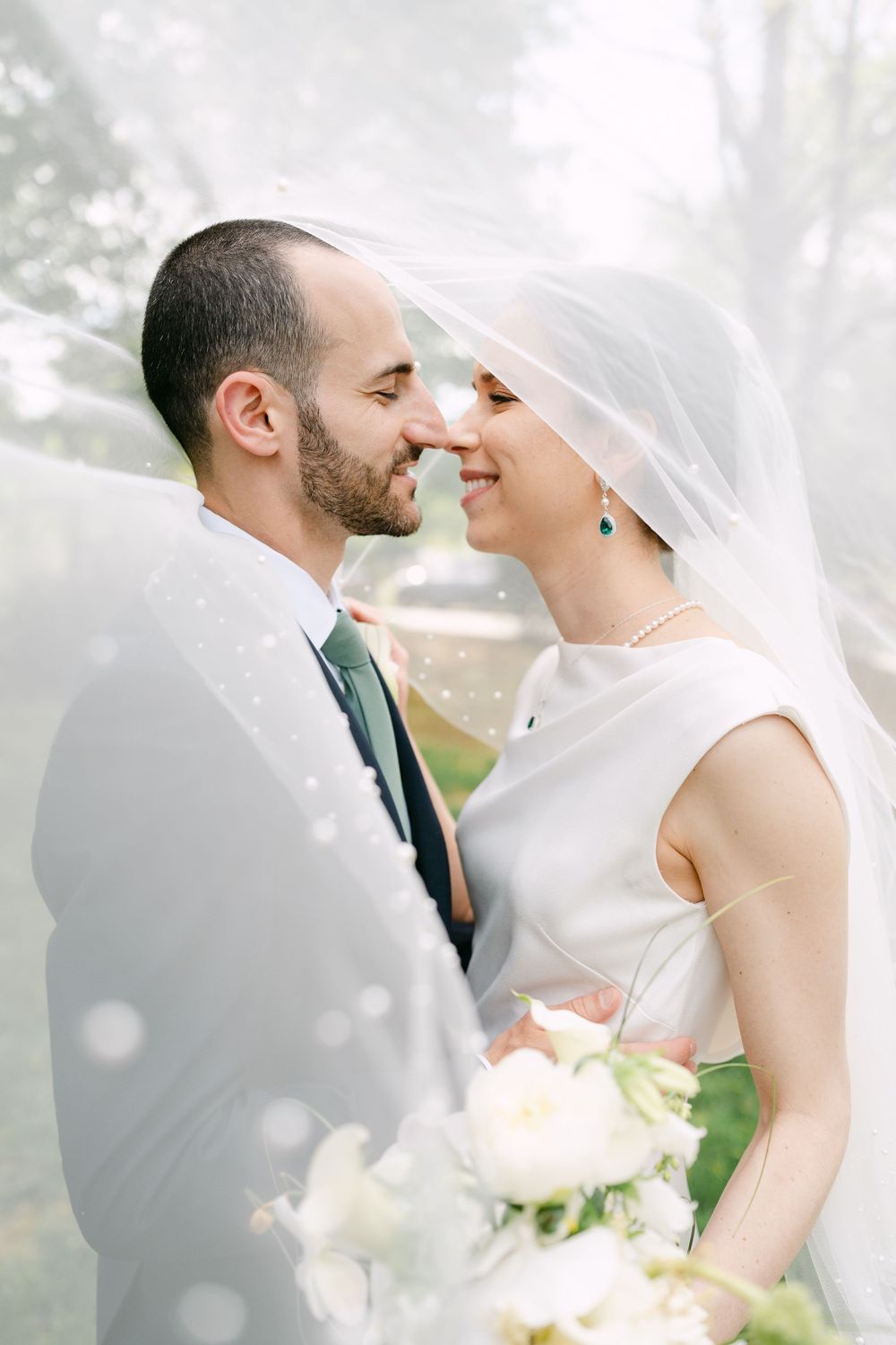 A tender wedding moment captured through soft veil with white roses in the foreground.