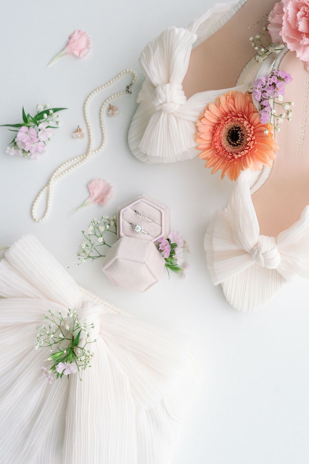 Elegant wedding details with white tulle, peach gerbera daisy, pearls and pink flowers arranged on light background.