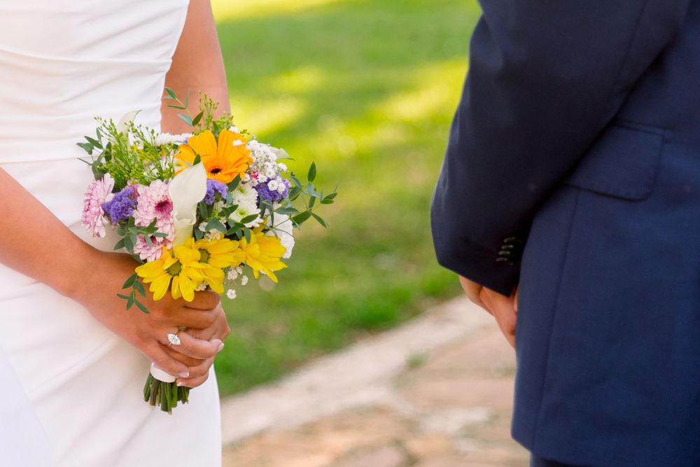 Wedding couple standing together outdoors with bride holding vibrant yellow and purple wildflower bouquet.