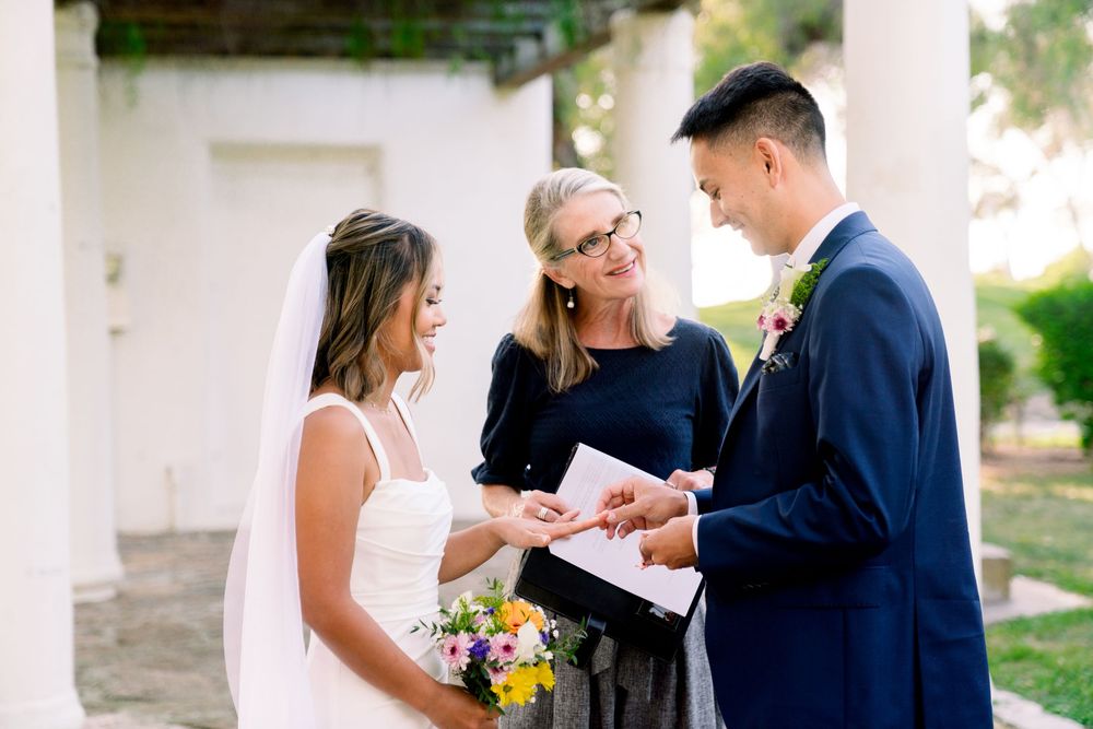 A wedding ceremony takes place under a covered outdoor walkway with a bouquet of yellow and white flowers.