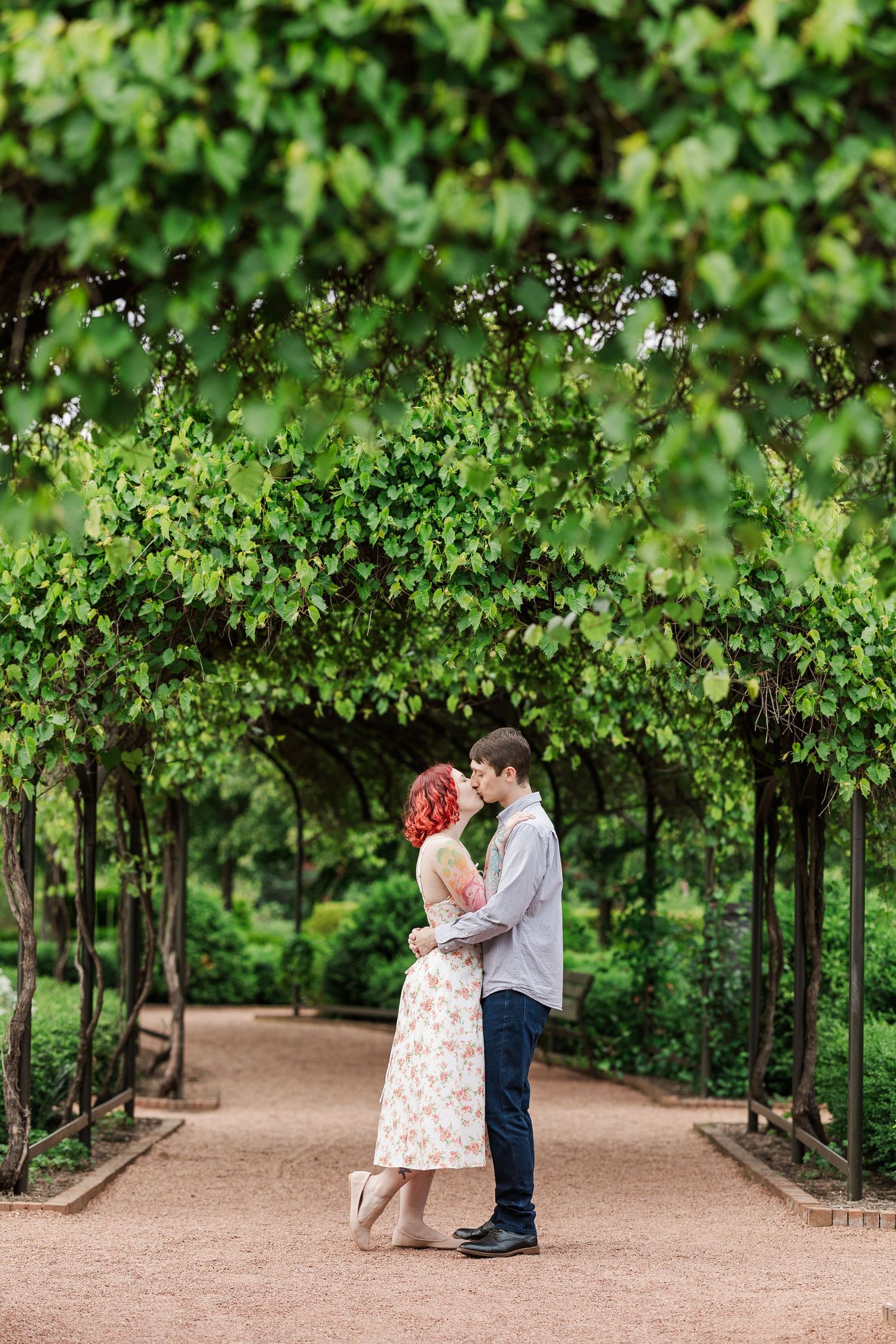 A couple shares a romantic moment under a lush green archway tunnel in a garden setting at Cantigny Park
