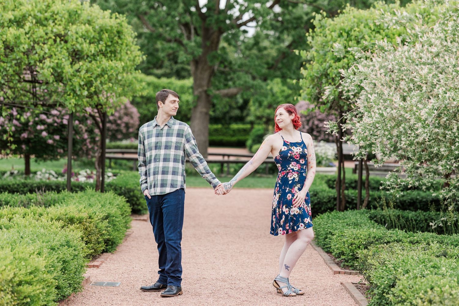 A couple embraces on a winding garden path surrounded by lush greenery and flowering trees in a peaceful park setting at Cantigny Park