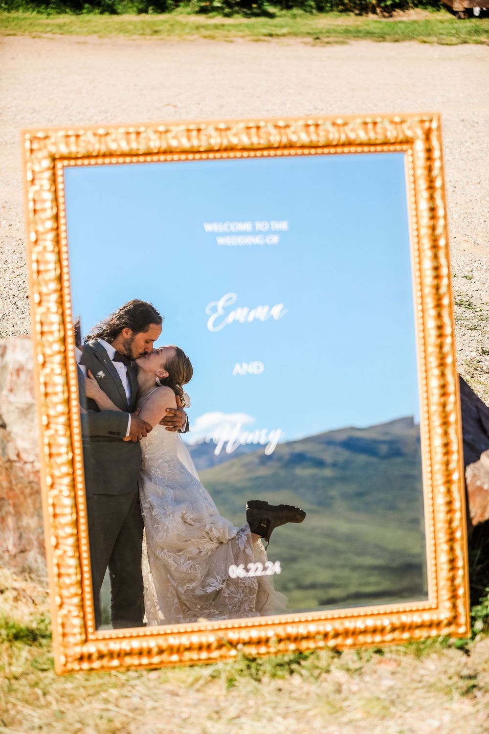 Couple's romantic portrait reflected in ornate gold mirror with mountain scenery.