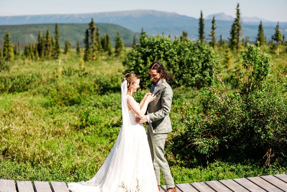 Couple shares romantic moment on wooden deck with mountain range backdrop.