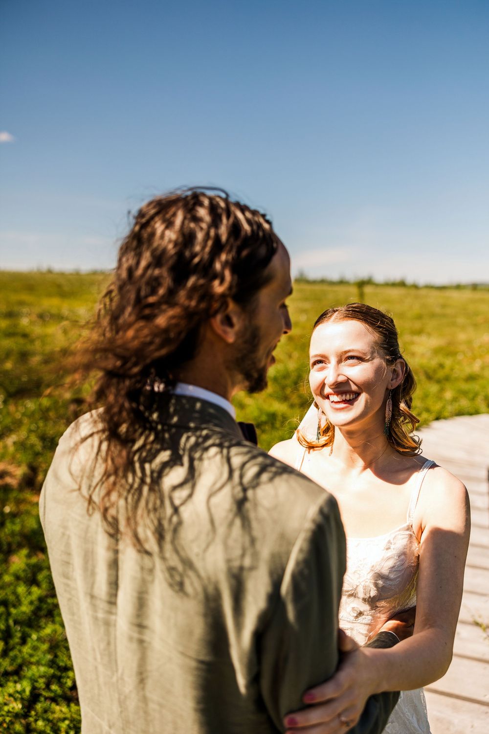 Bride laughs joyfully during intimate moment with partner in sunny outdoor setting.