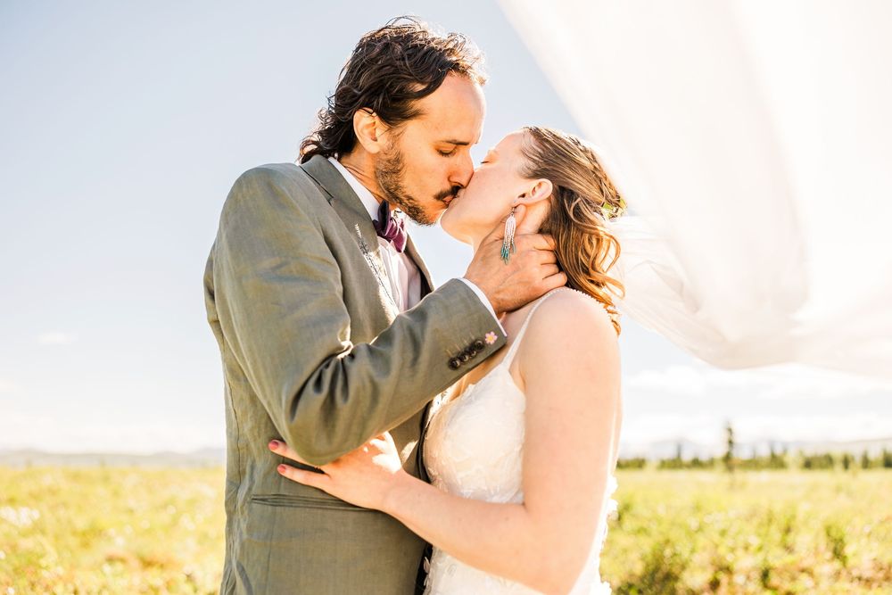 Romantic wedding portrait captures tender kiss in sunny mountain landscape.