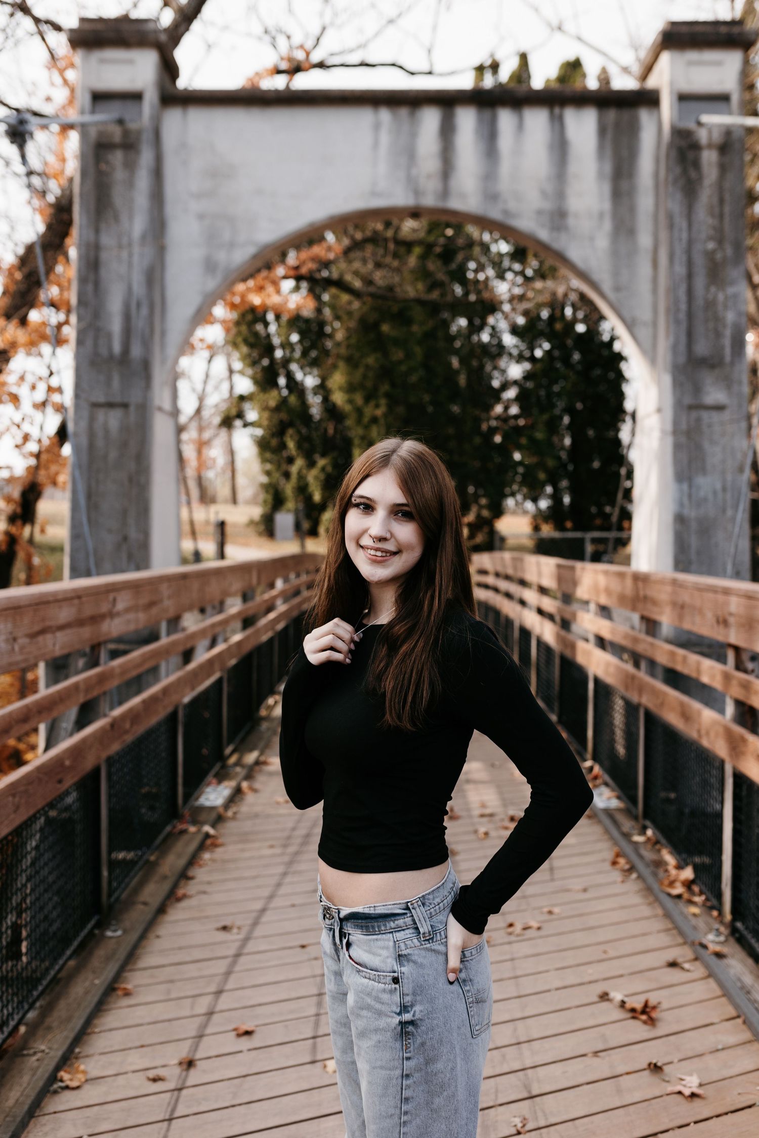 Portrait on a wooden bridge with stone archway entrance surrounded by autumn foliage.