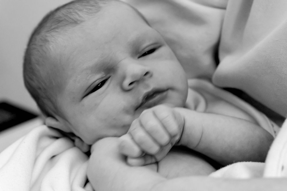 Black and white portrait of a sleeping newborn infant resting with hand near face wrapped in soft bedding.