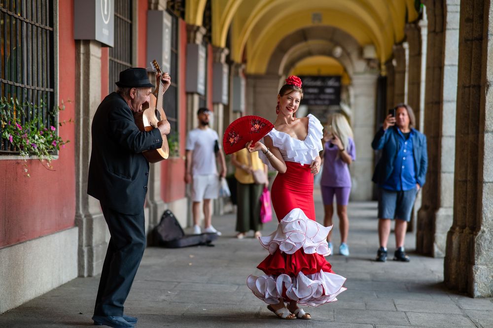 A photographer captures a flamenco dancer in a red and white ruffled dress twirling under a historic Spanish archway.