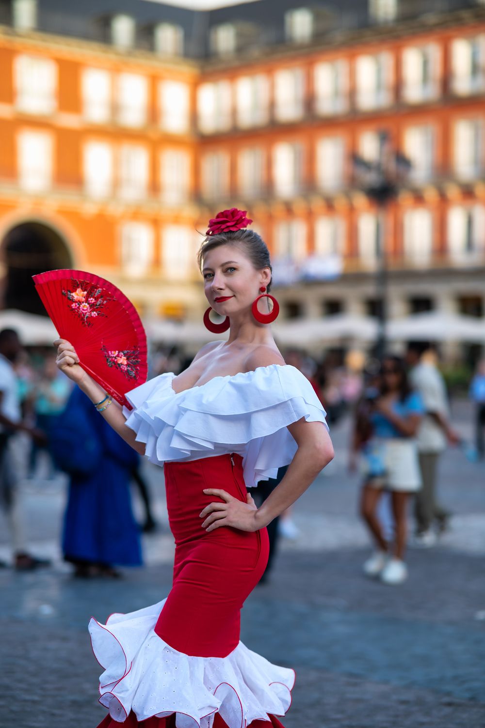 Flamenco dancer in traditional red and white dress poses with fan in Madrid's Plaza Mayor.