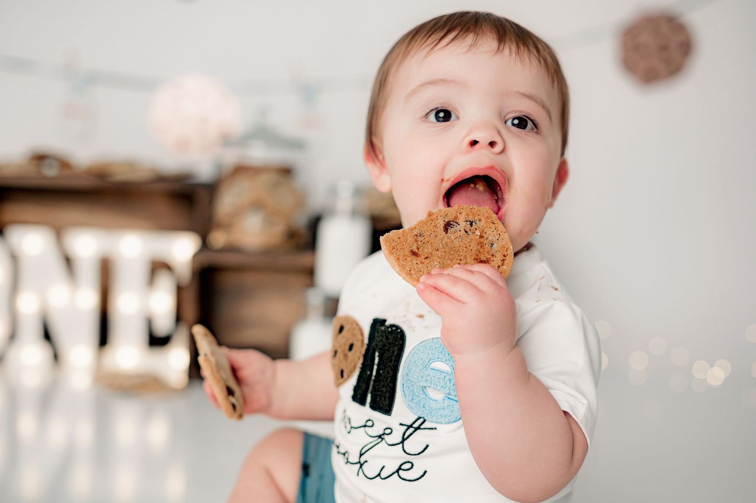 First birthday photo setup with wooden crates, 'ONE' letters, cookies, and 'one sweet boy' banner against white backdrop.