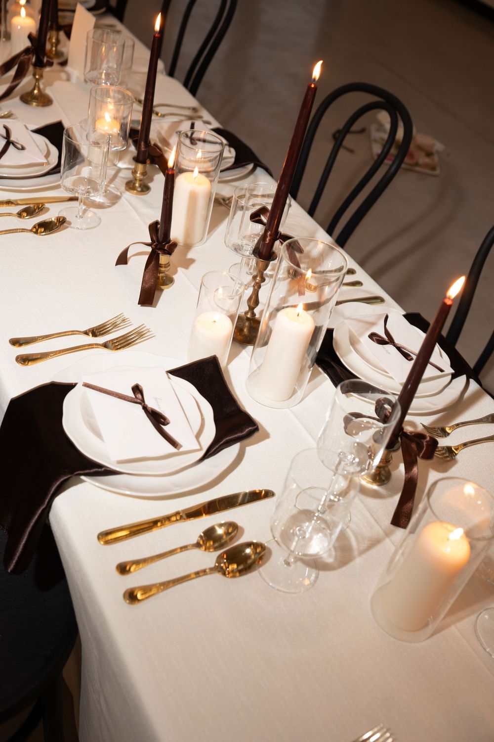 Elegant table setting with gold cutlery, white linens, and glowing candles creating a romantic fine dining atmosphere.