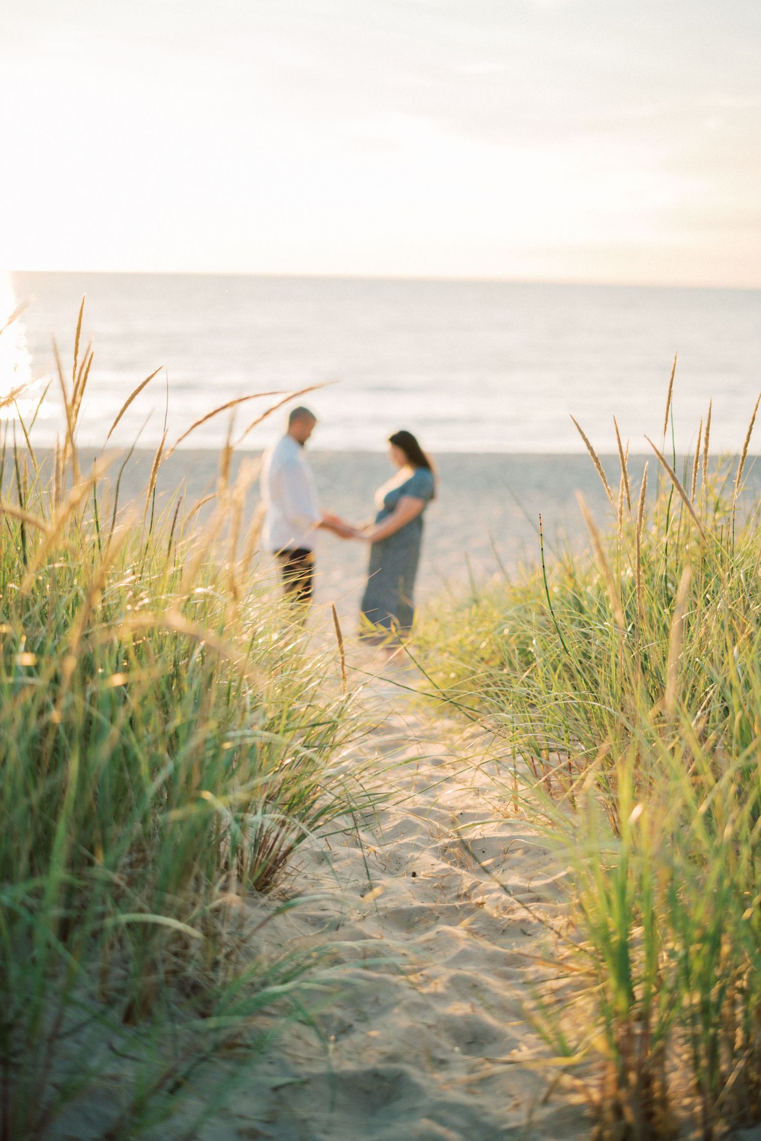 Romantic couple silhouetted at sunset among beach grass dunes near the ocean.