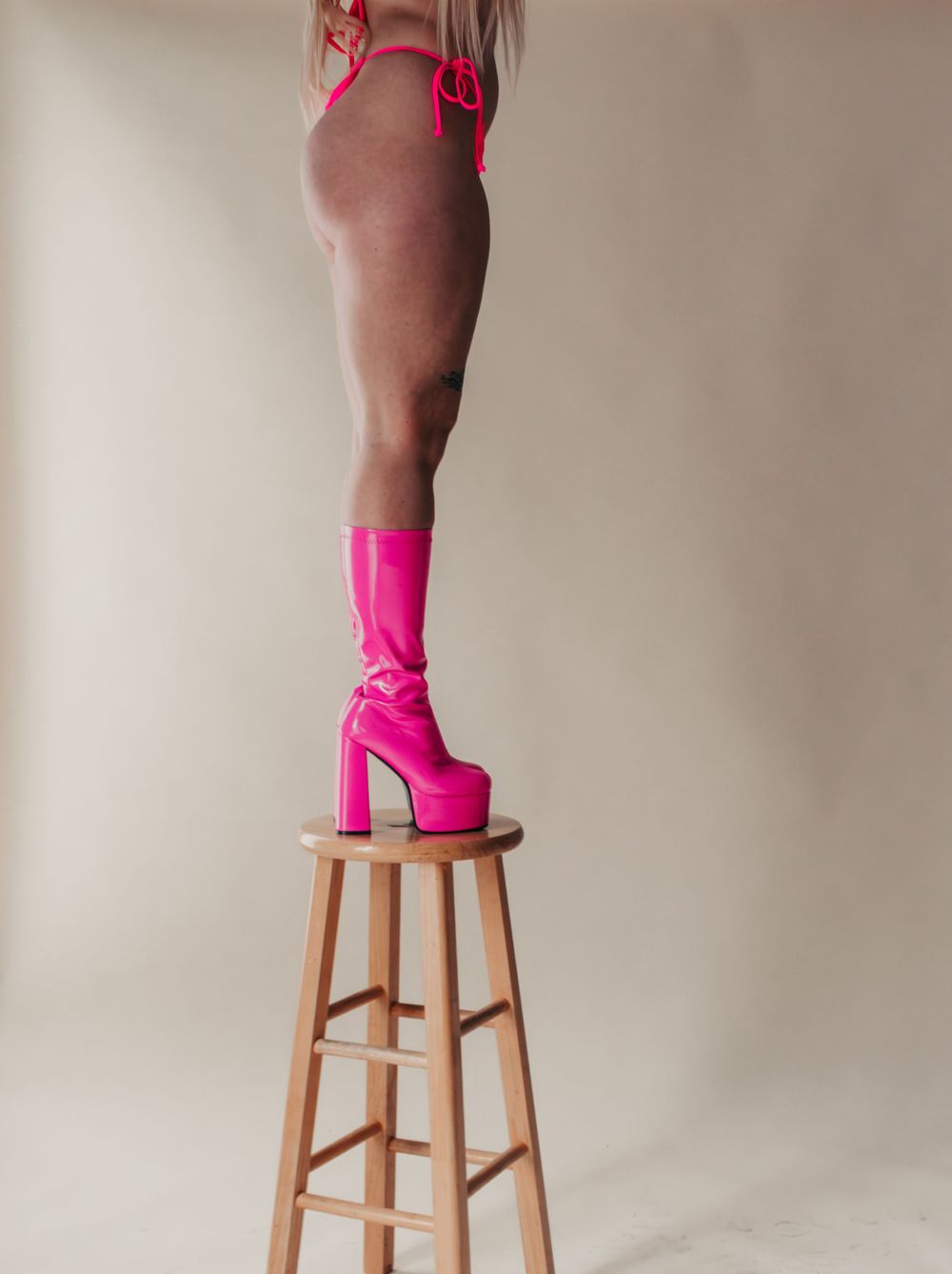 Studio Boudoir
Person standing on wooden stool wearing vibrant hot pink platform boots and bikini swimwear against neutral background.