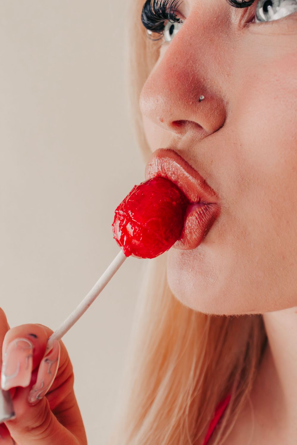 Studio Boudoir Photoshoot
Close-up detail of red heart-shaped lollipop candy being held up to glossy red lipstick-painted lips.