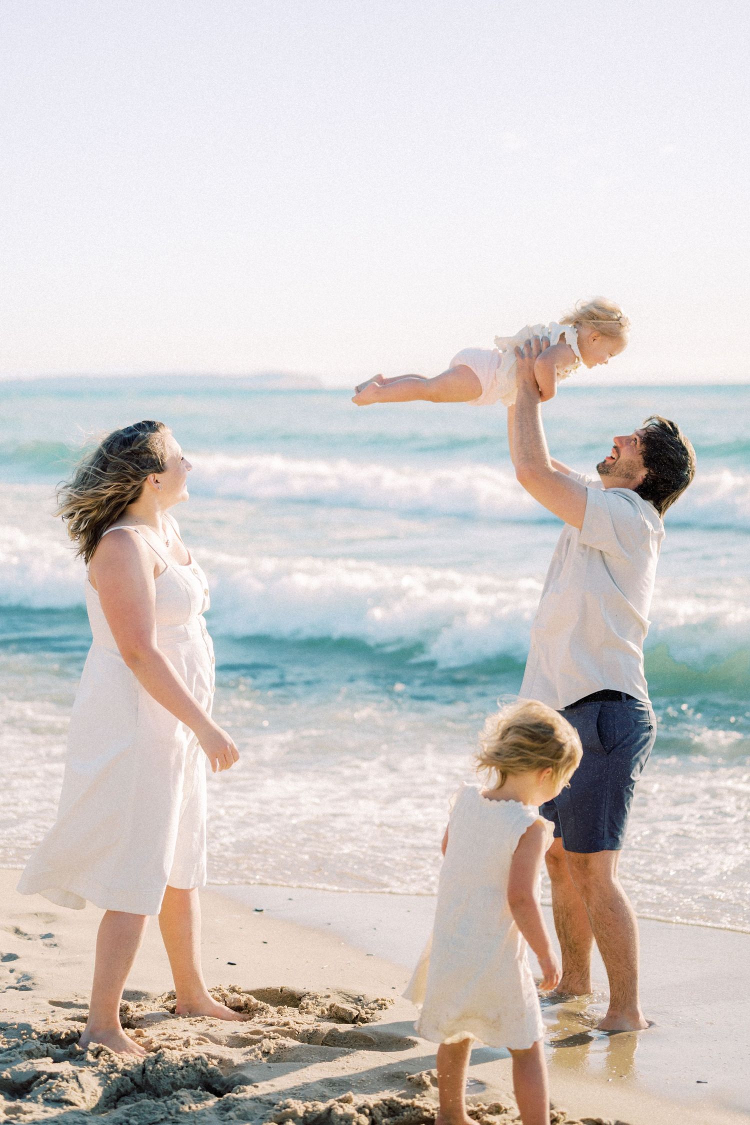 A joyful beach scene with waves crashing as a family plays together in the sand.